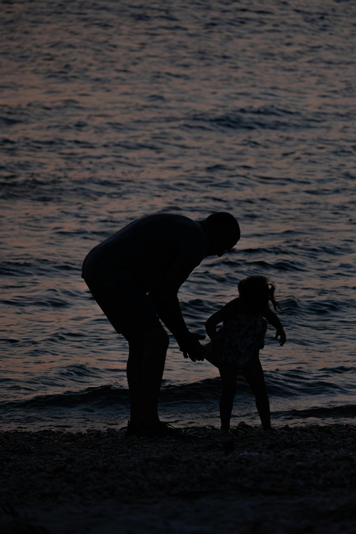 父と幼い娘の海辺の夕暮れシルエット