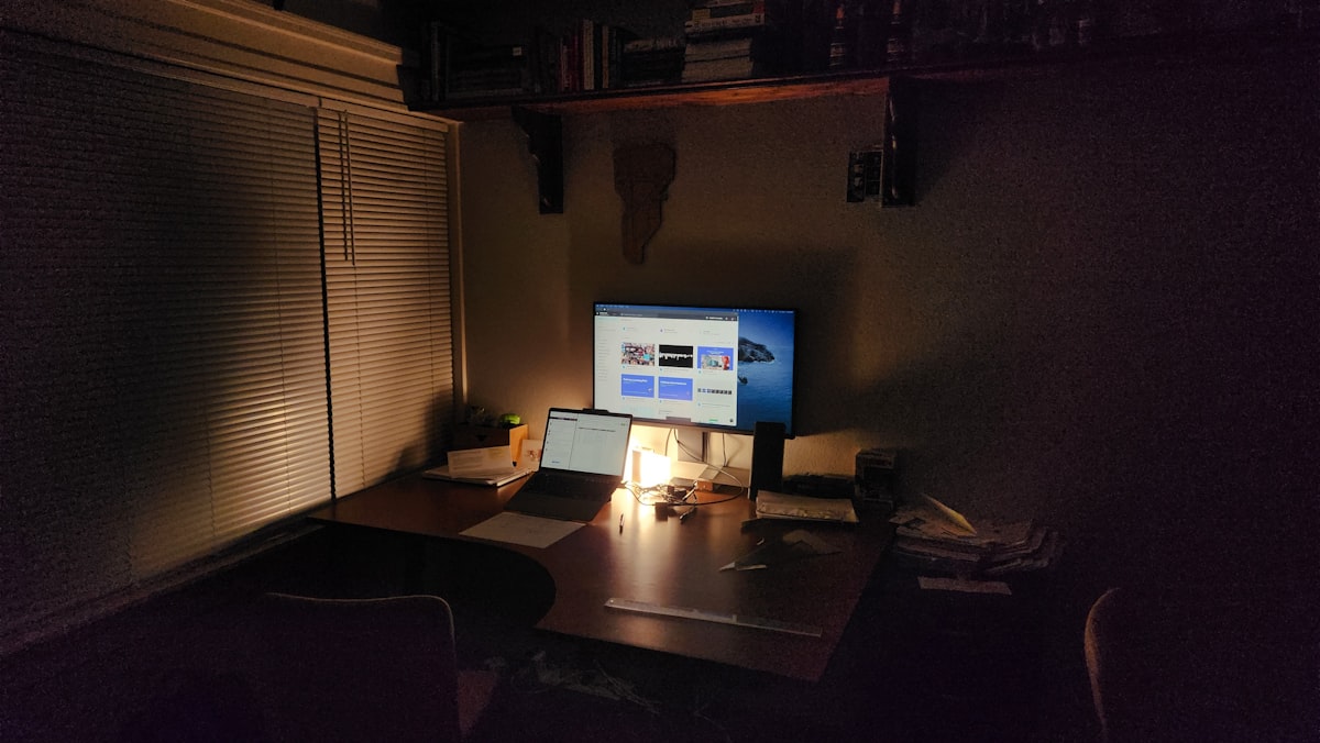 暗い部屋のデスク・モニター・MacBook・夜の窓辺