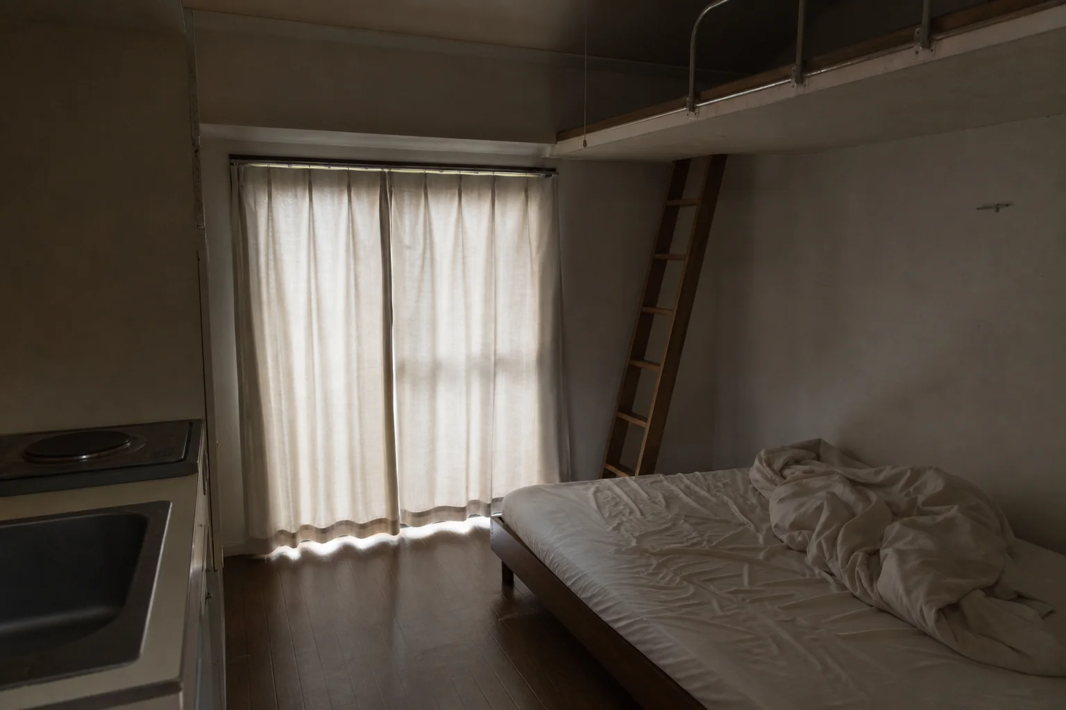 カーテンを閉め切った安アパートの部屋とベッド