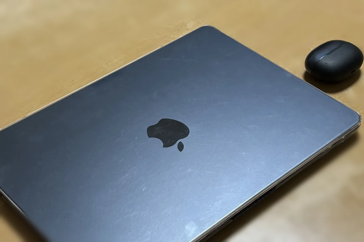 机の上の閉じたMacBook Air（リンゴマーク入り）とShokzのイヤホンケース・実物