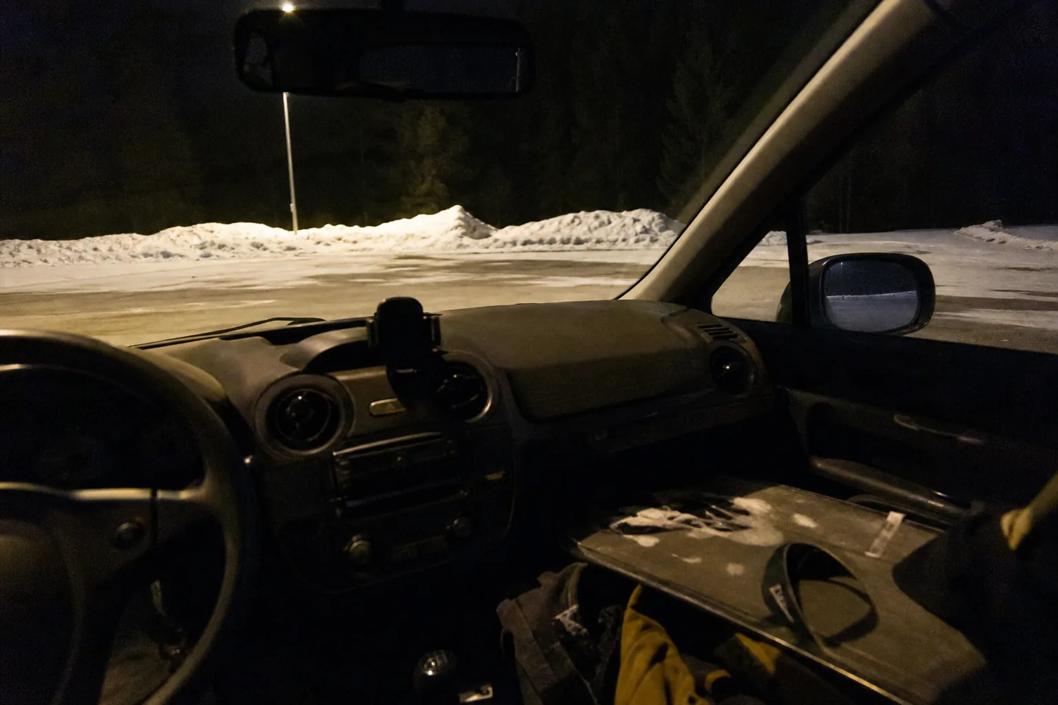 雪の夜の駐車場で停車中、運転席から見た無人の車内。助手席にスノボ板1枚