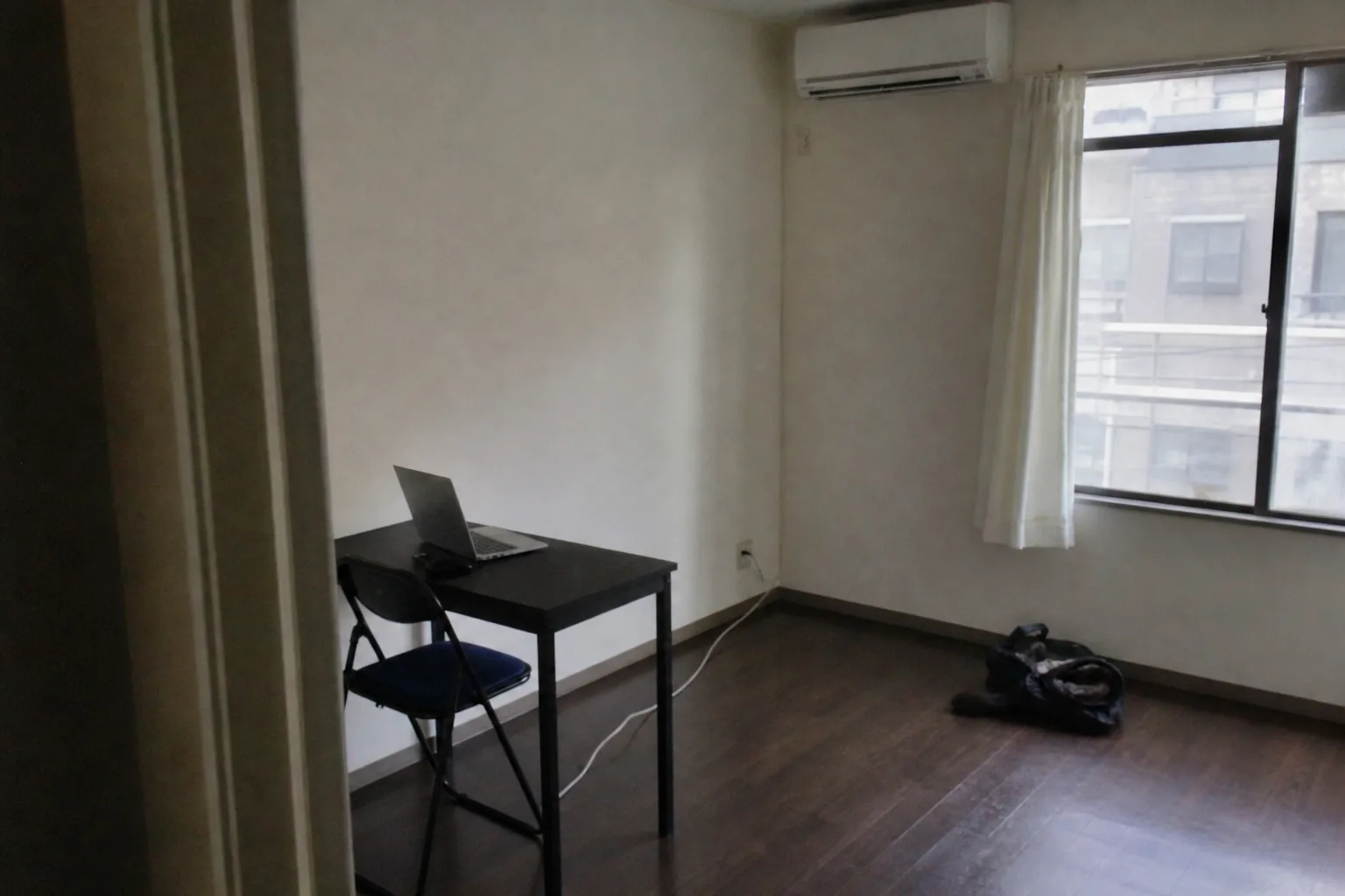 物がほぼ無い部屋、小さな机と椅子とノートPCだけ、昼の光