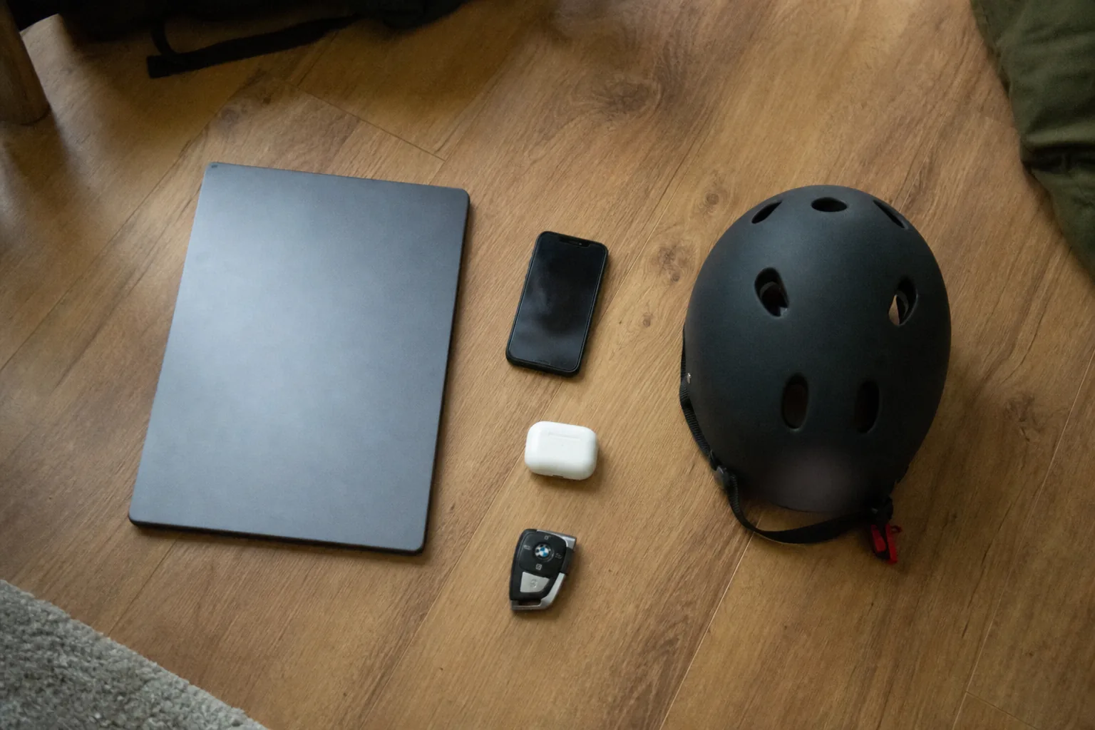 フローリングに並べた毎日使う物一式（ノートPC・スマホ・イヤホンケース・バイクのヘルメット・車のキー）俯瞰