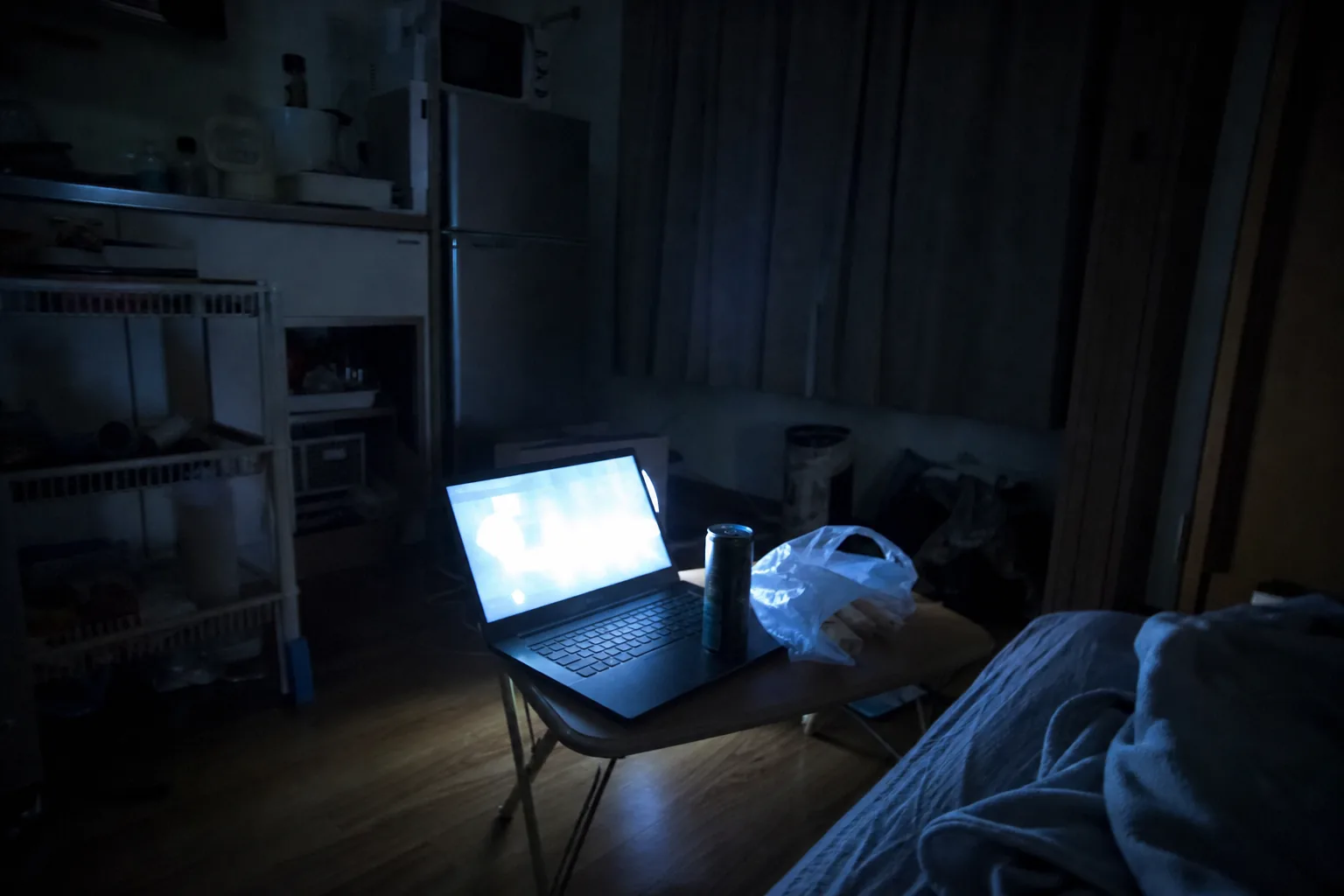 深夜の狭いワンルーム、折りたたみ机のノートPCの青白い光だけ。畳と掛け軸なし