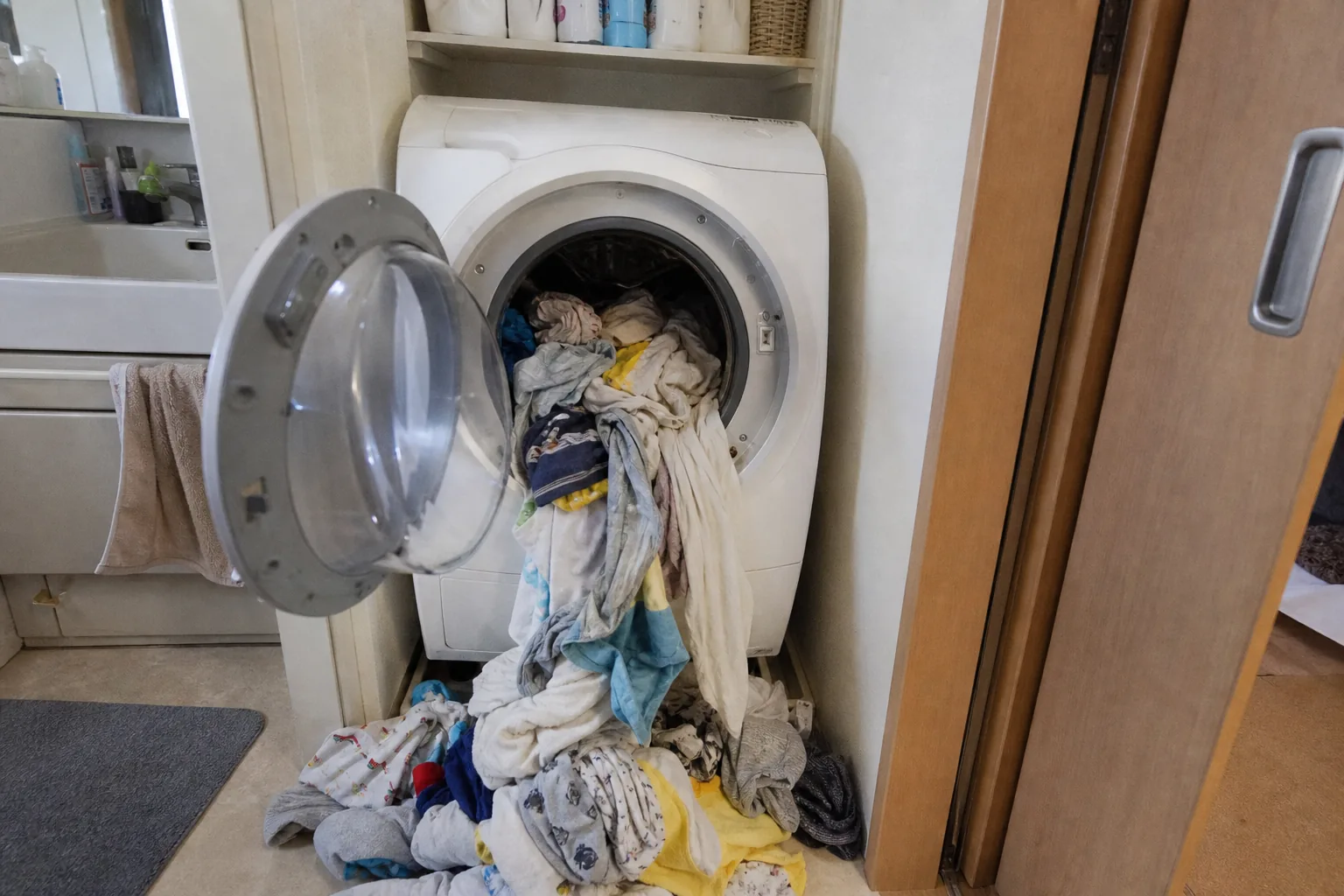 狭い洗面所のドラム式洗濯乾燥機、扉が開いて子ども服がこぼれ出た瞬間
